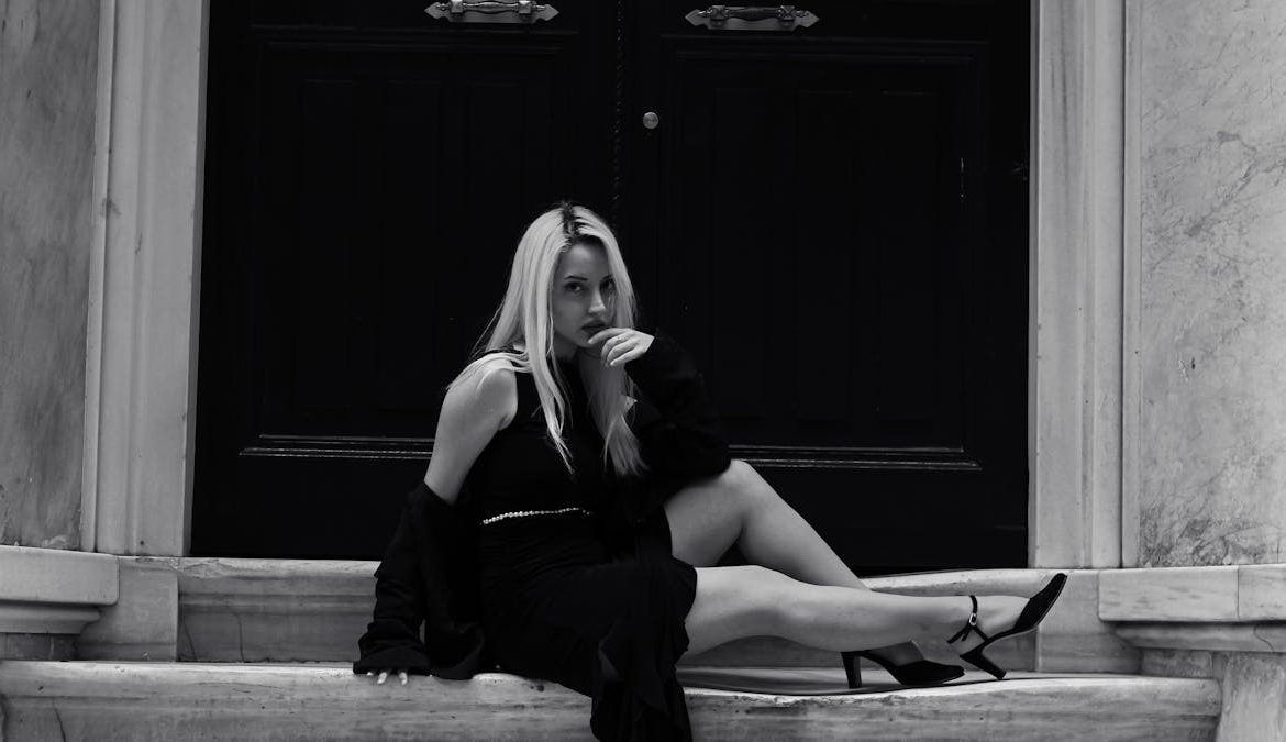 Elegant black and white portrait of a woman in urban fashion sitting on steps.