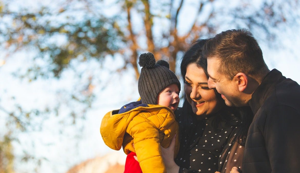 Child in parents arms looking at them, all laughing.